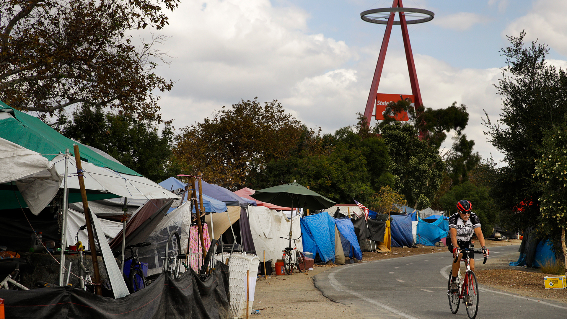 n this Sept. 14, 2017 file photo a cyclist passes the row of tents and tarps along the Santa Ana riverbed near Angel Stadium in Anaheim, Calif.  (AP Photo/Jae C. Hong, File)